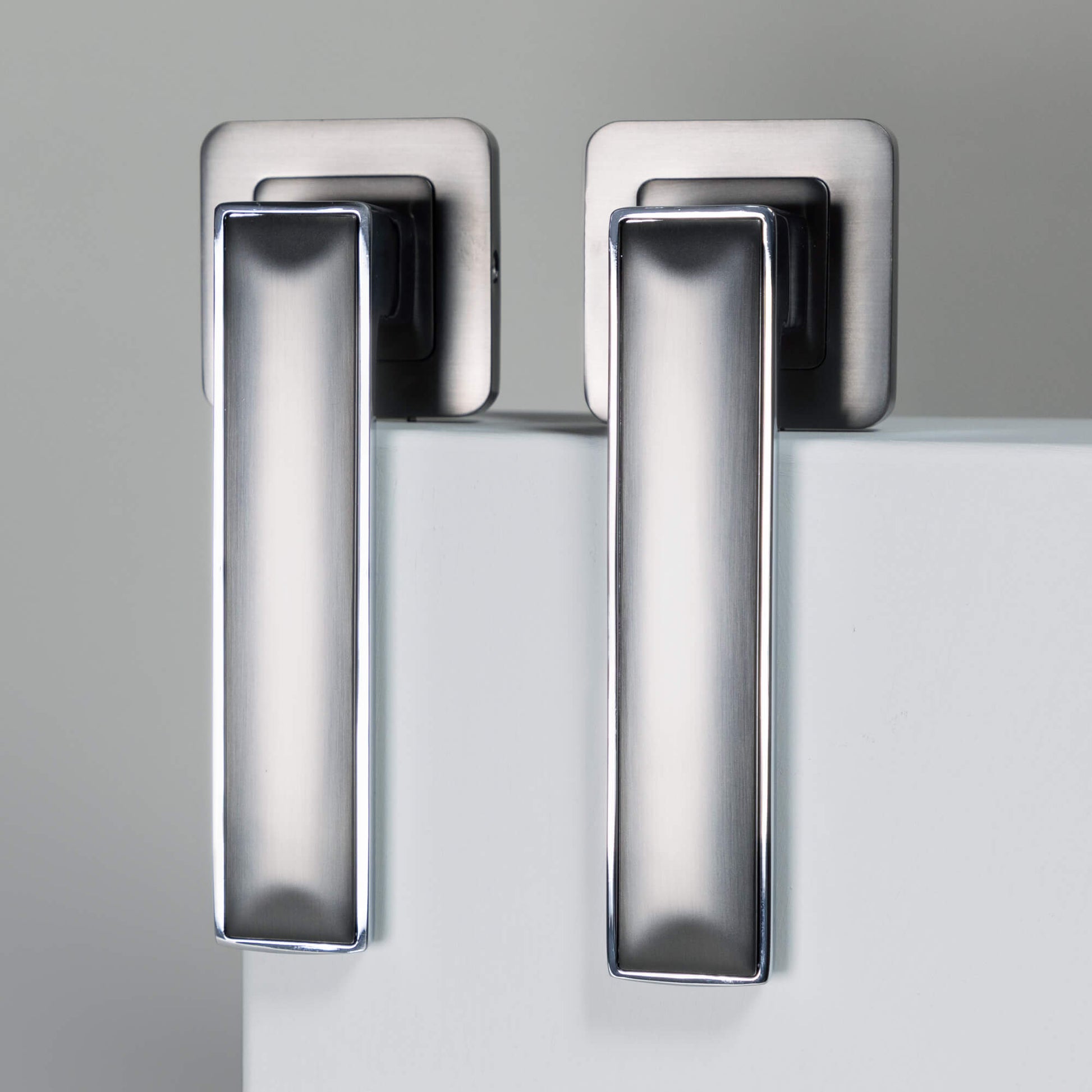 A set of Alto Nickel Brushed & Polished Chrome Square Rose Handles on a grey background