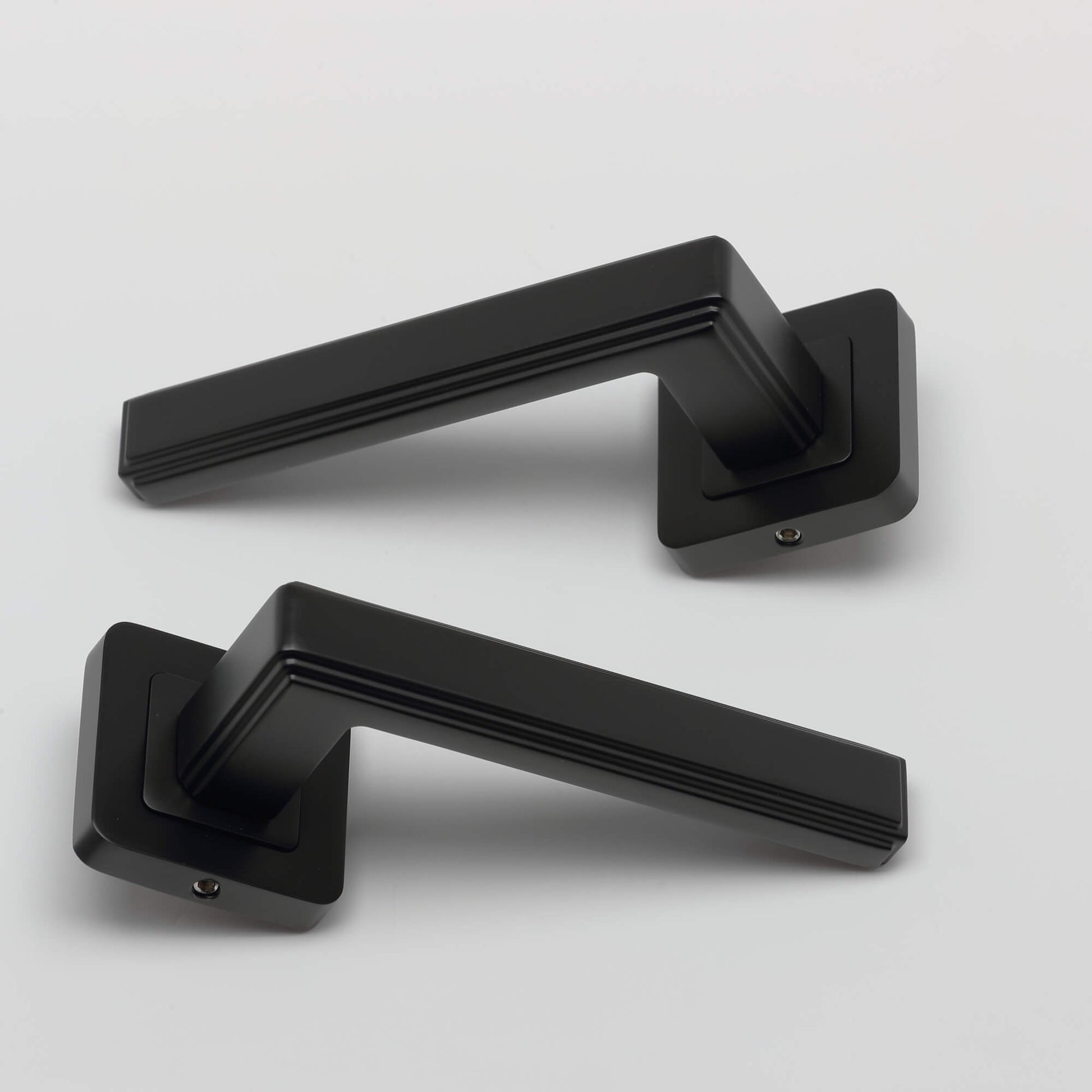 A set of Ares Flat Black Square Rose door handles on a grey background.