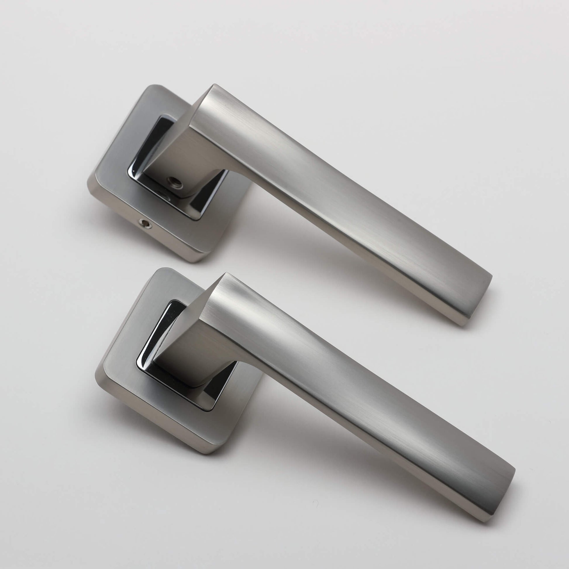 An angled view of an Artemis Matt Satin Nickel & Polished Chrome Square Rose door handle on a light grey background.