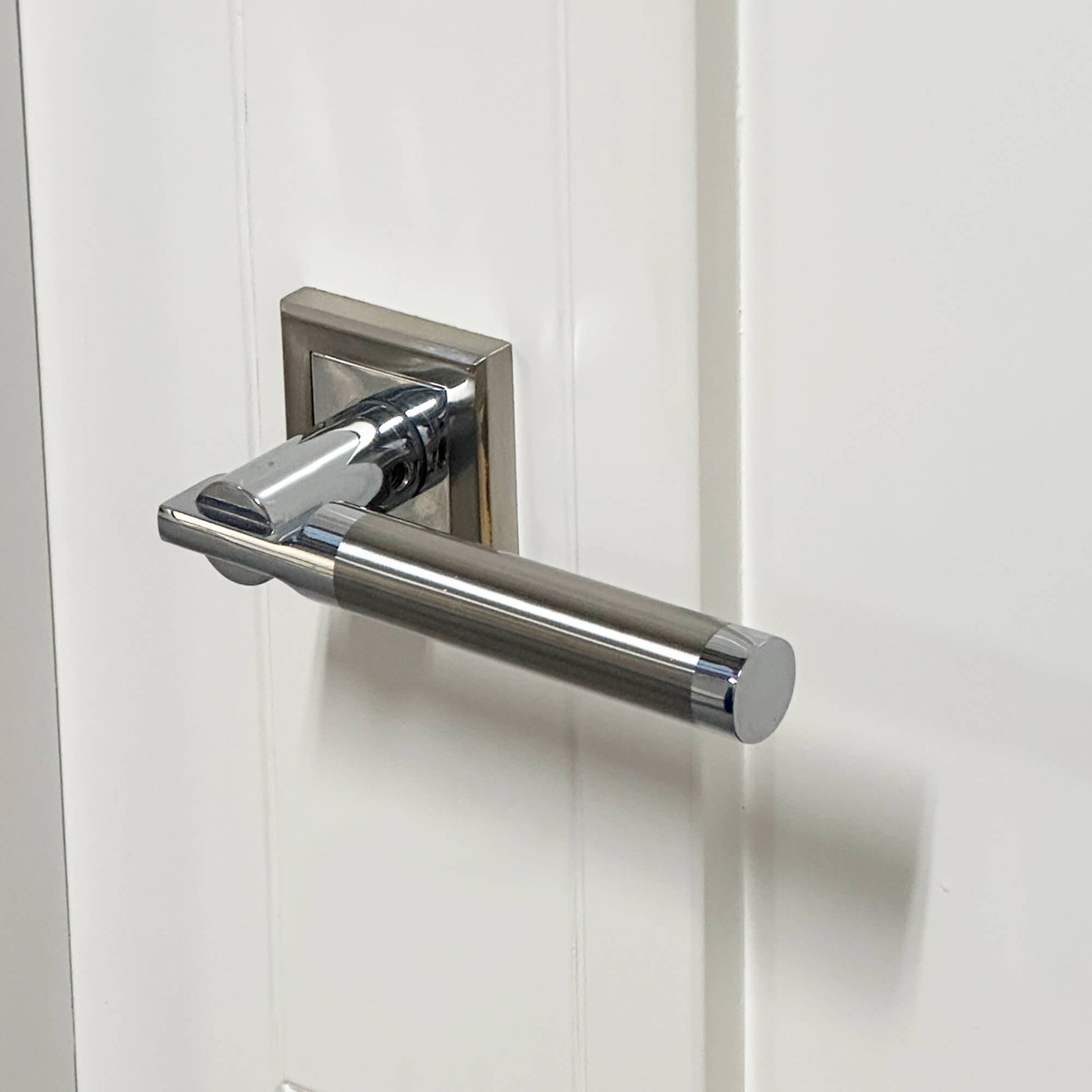 A Cumulus Nickel Brushed & Polished Chrome Square Rose Handle on a white wooden door