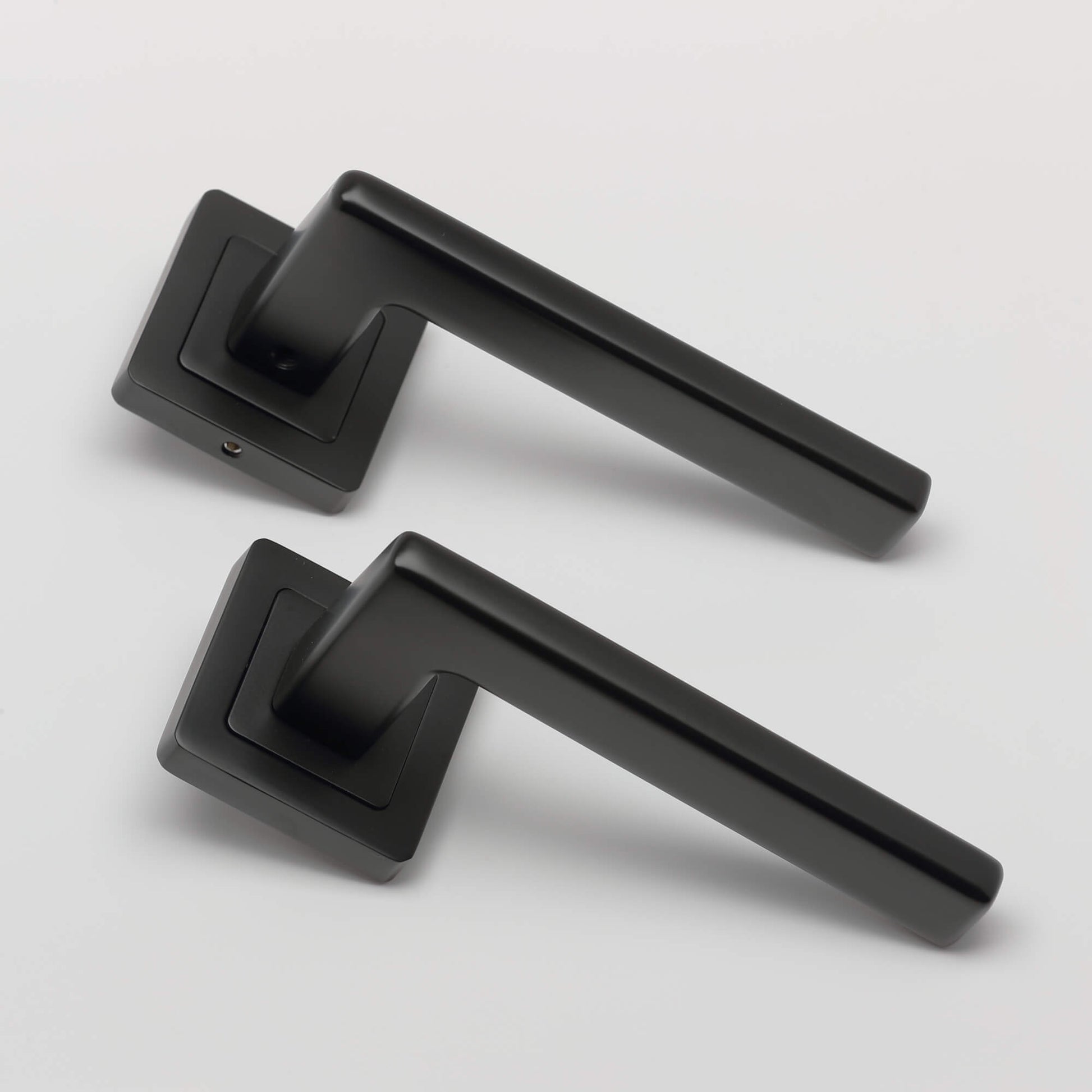 An angled view of a set of Hera Flat Black Square Rose door handles on a light grey background.