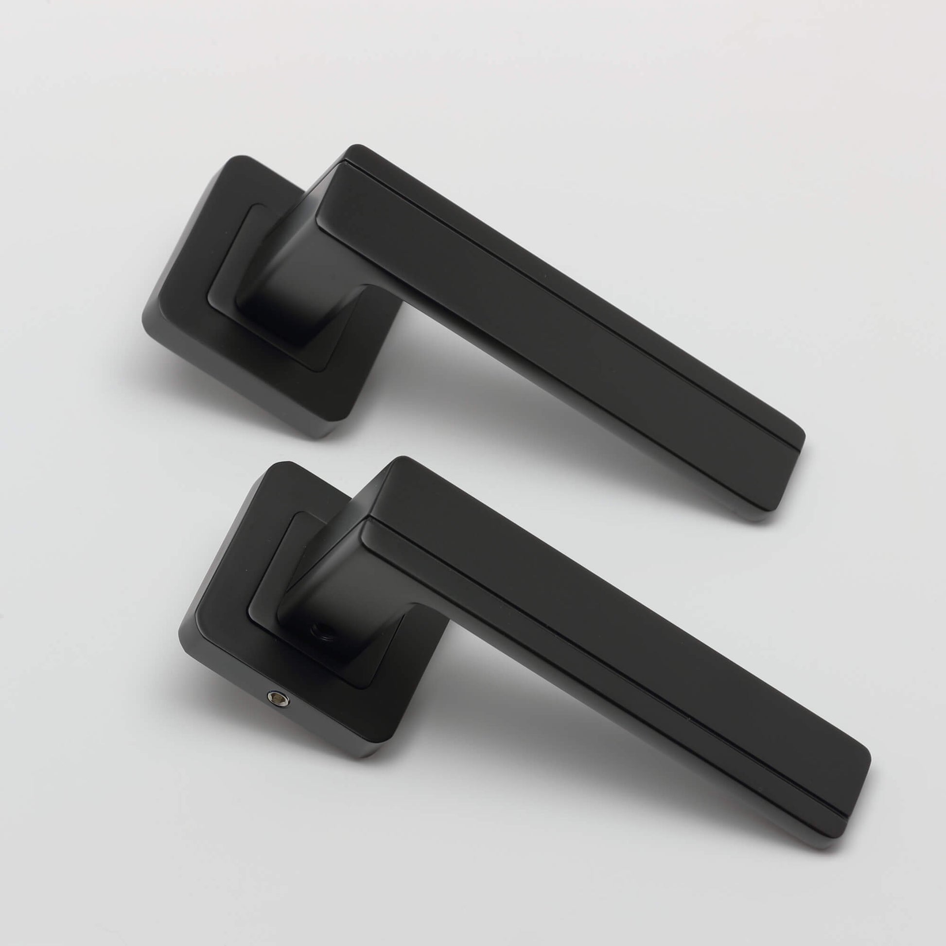 An angled view of a pair of Hermes flat black square rose door handles on a light grey background.