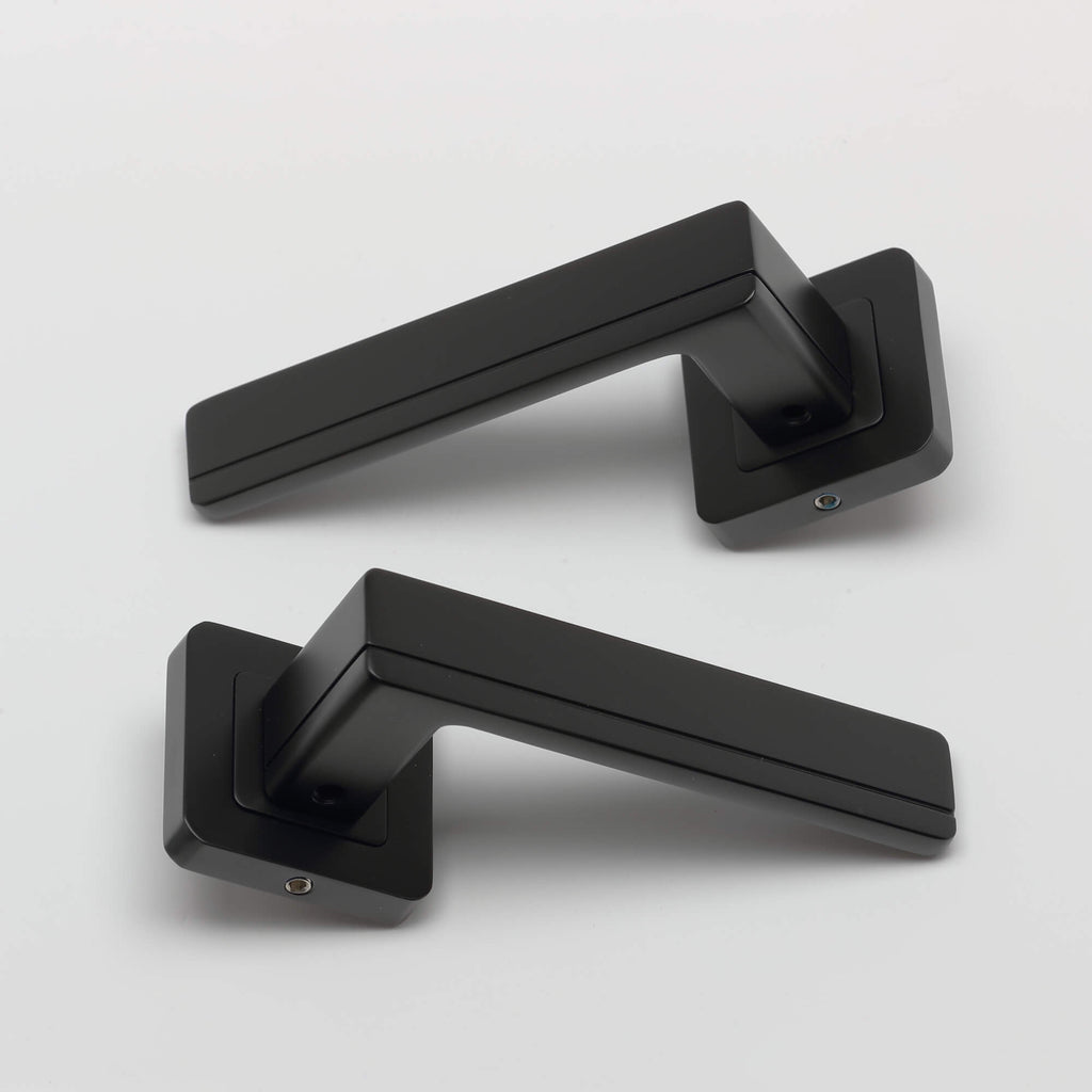 A pair of Hermes flat black square rose door handles on a light grey background.
