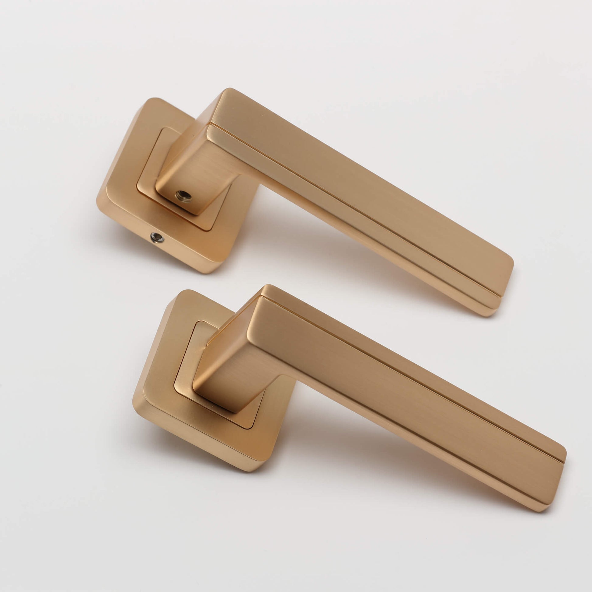 An angled view of a pair of Hermes Satin Brass Square Rose door handles on a white background.