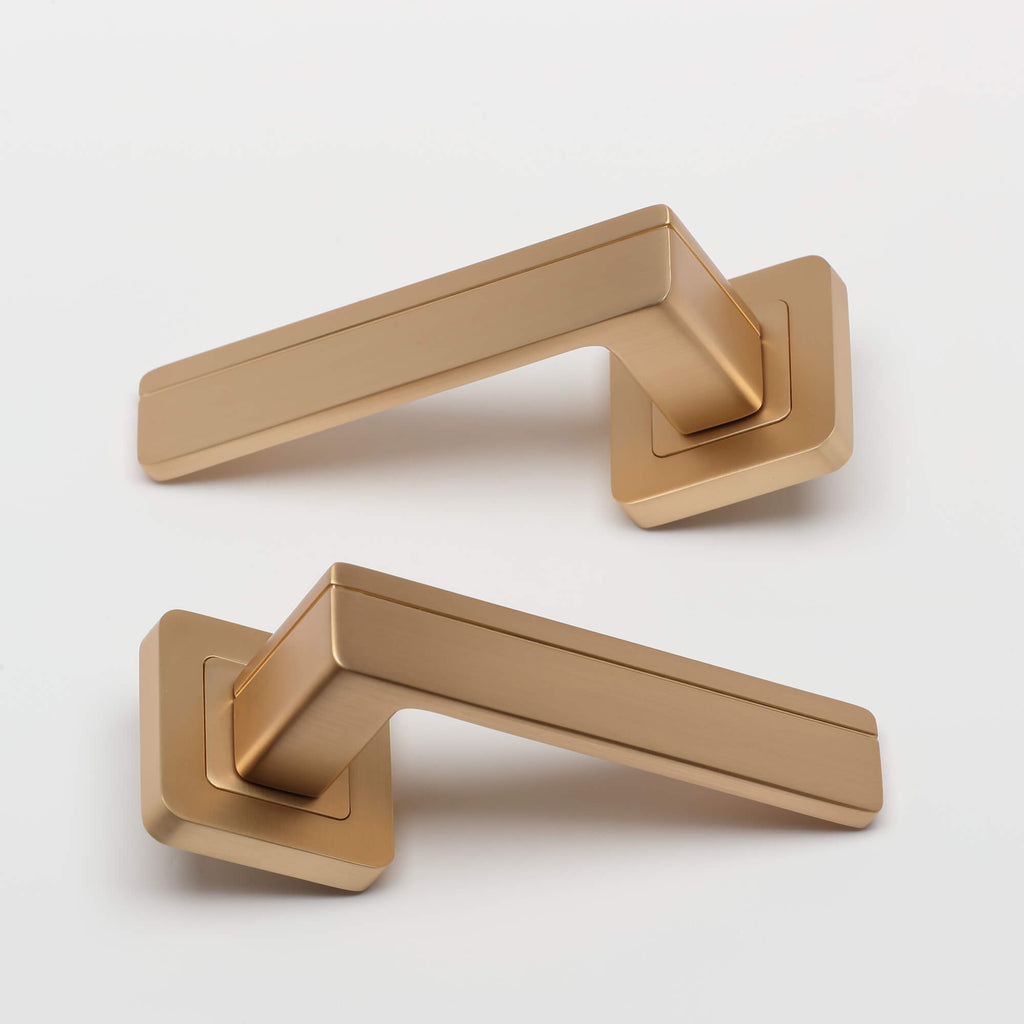 A pair of Hermes Satin Brass Square Rose door handles on a white background.