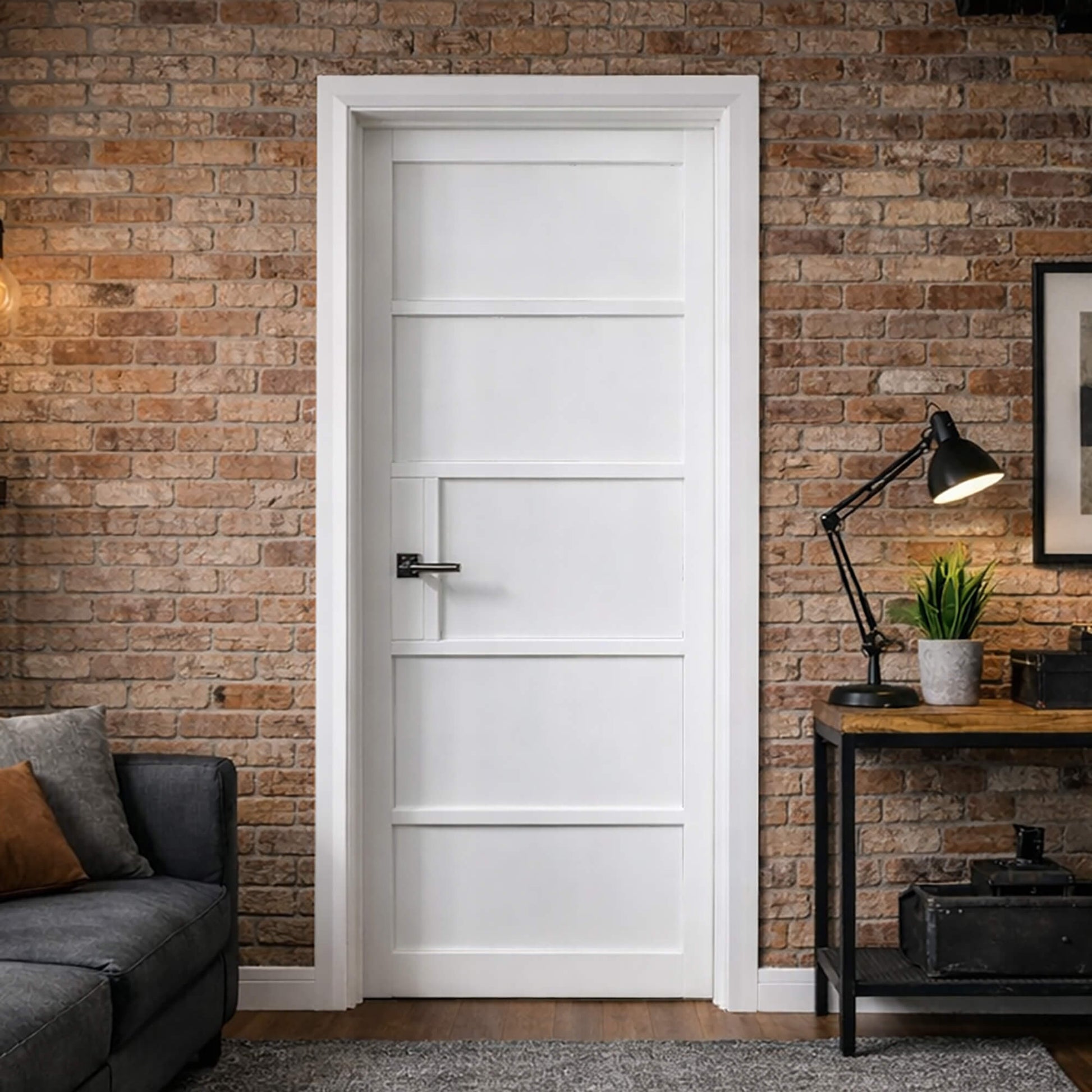 The Kew White Primer Plus 5 Panel Door in a living room  interior setting with a brick wall, grey sofa, and desk lamp.