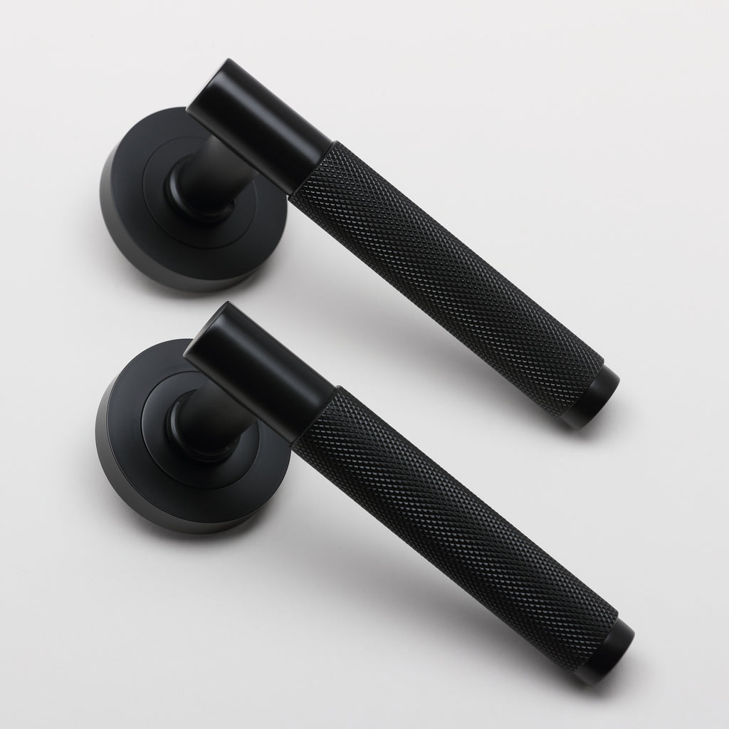 An angled view of a pair of Knurled Flat Black door handles on a grey background.
