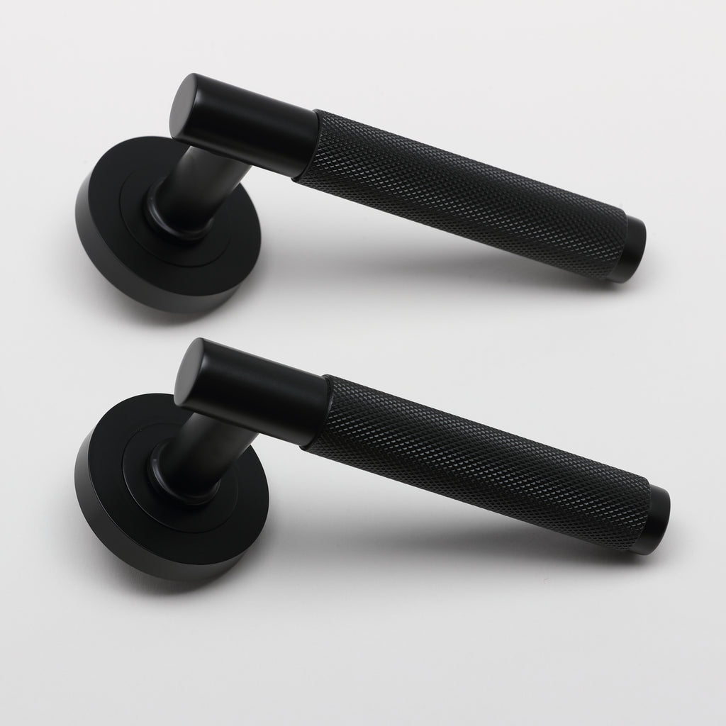 A side view of a pair of Knurled Flat Black door handles on a grey background.