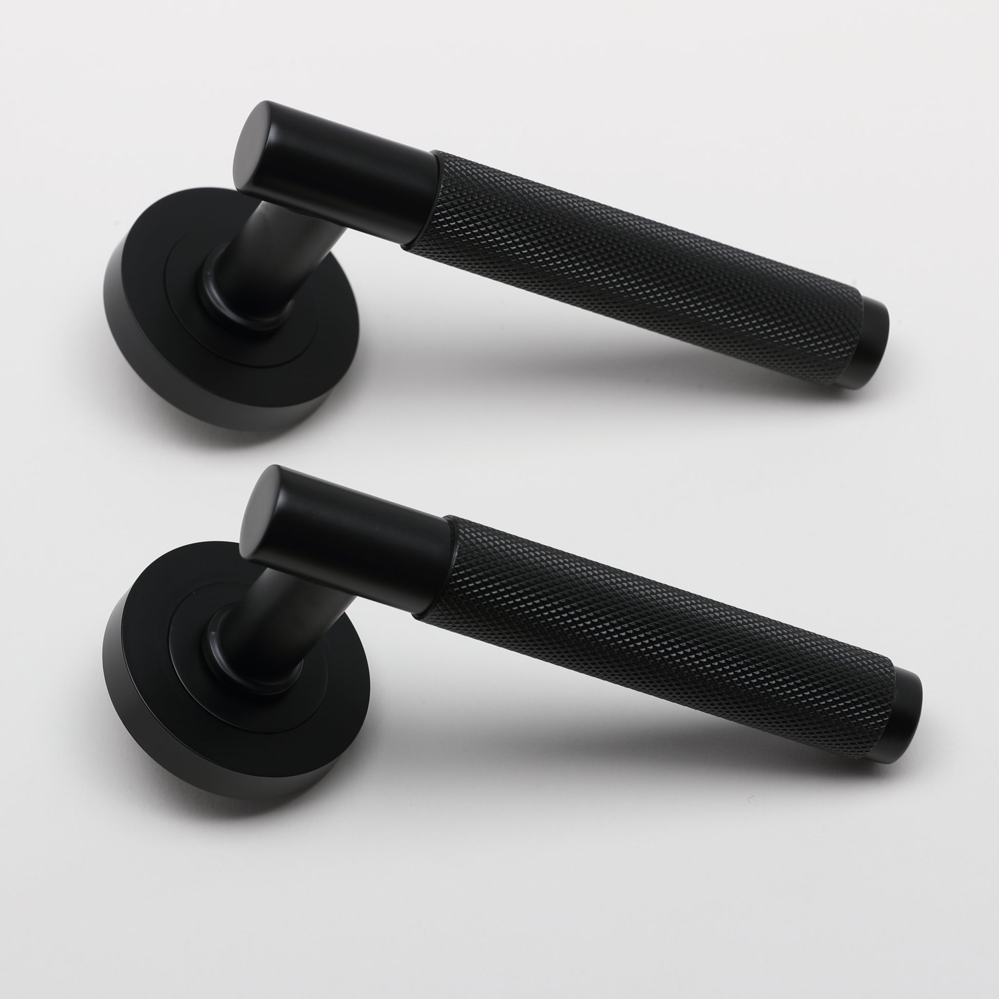 A side view of a pair of Knurled Flat Black door handles on a grey background.