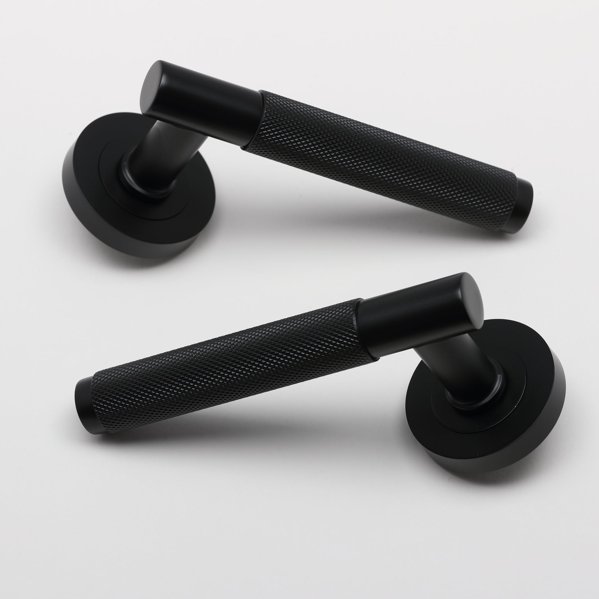 A pair of Knurled Flat Black door handles on a grey background.
