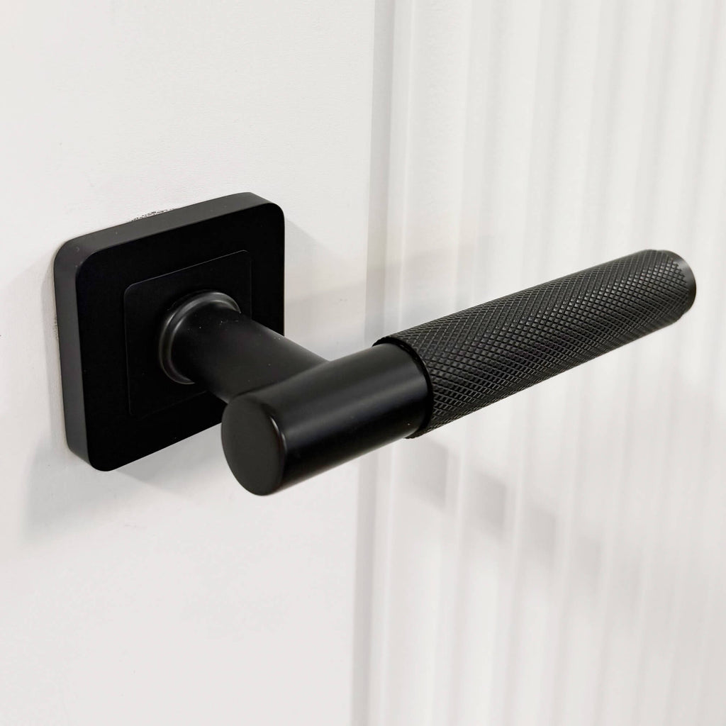 Close-up of a Knurled Flat Black Square Rose door handle on a White Primed Reeded Door
