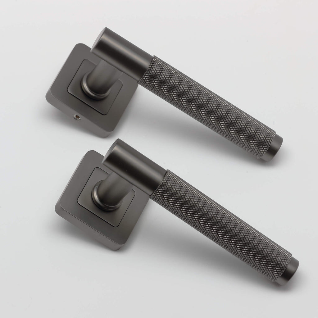 An angled view of a pair of Knurled Matt Satin Black Square Rose Door Handles on a grey background.