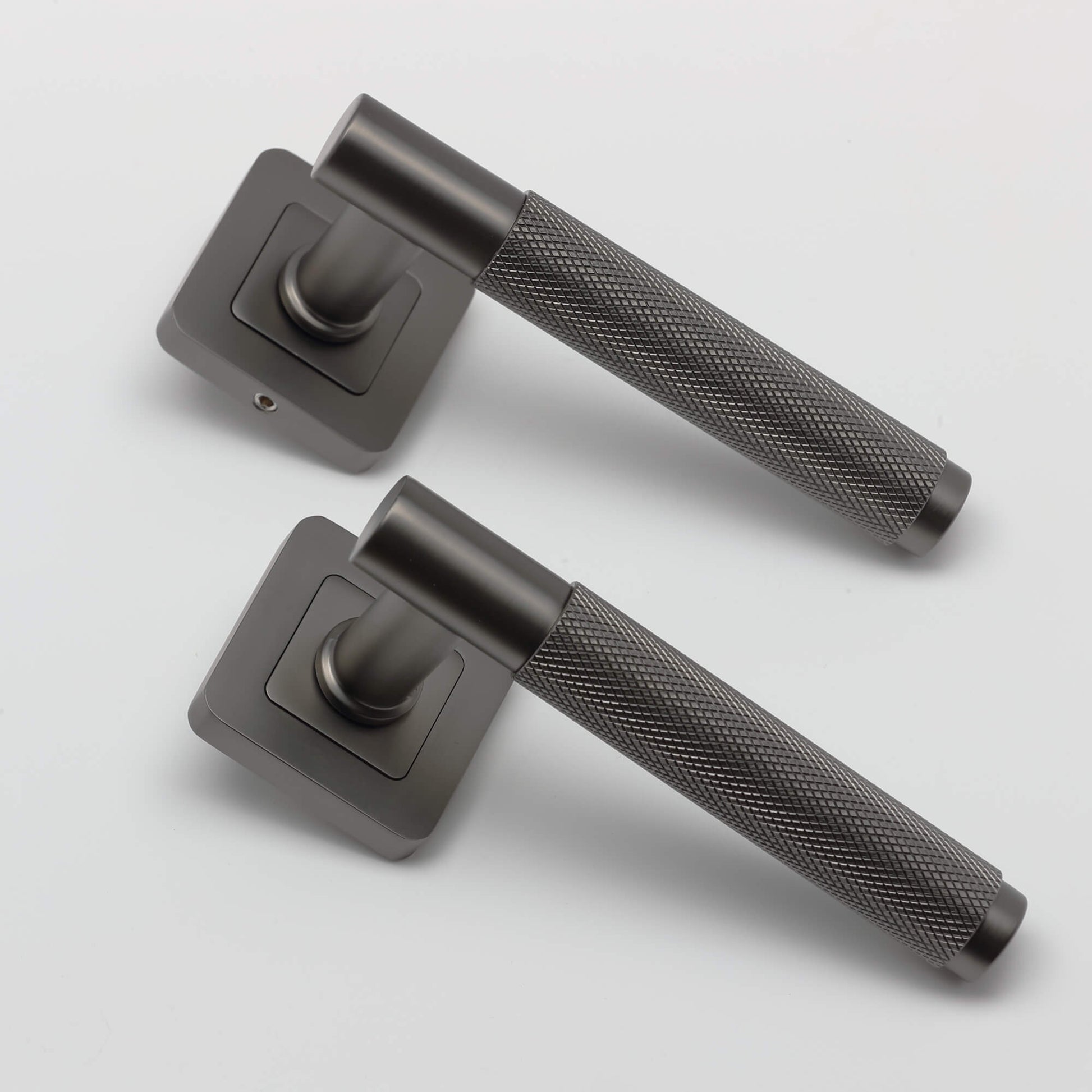 An angled view of a pair of Knurled Matt Satin Black Square Rose Door Handles on a grey background.