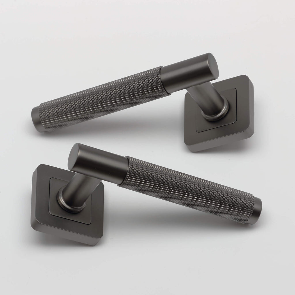 A set of Knurled Matt Satin Black Square Rose Door Handles on a grey background.