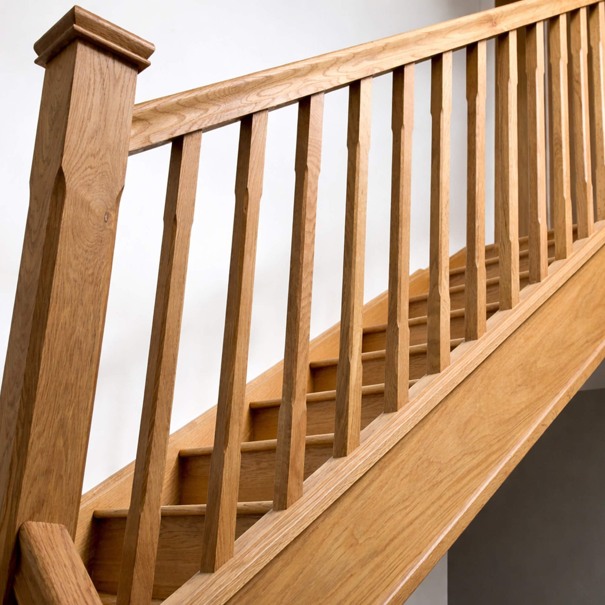 Close-up of Oak Chamfered Spindles with a chamfered newel post on a oak staircase with handrail against a white wall.