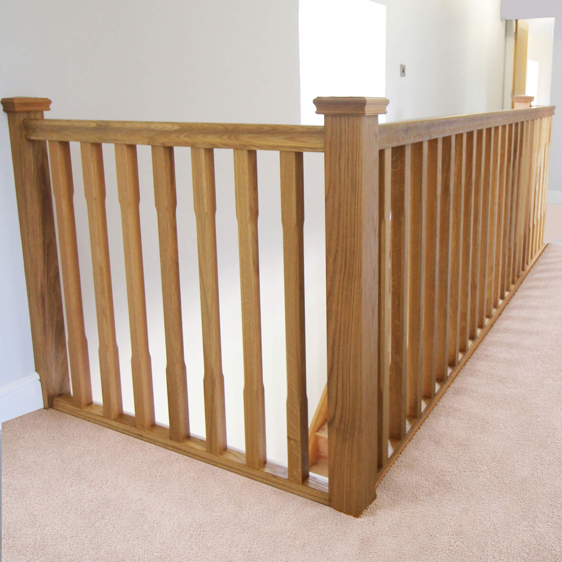 An oak staircase with Oak Chamfered Spindles in a home upstairs landing setting with a neutral background.