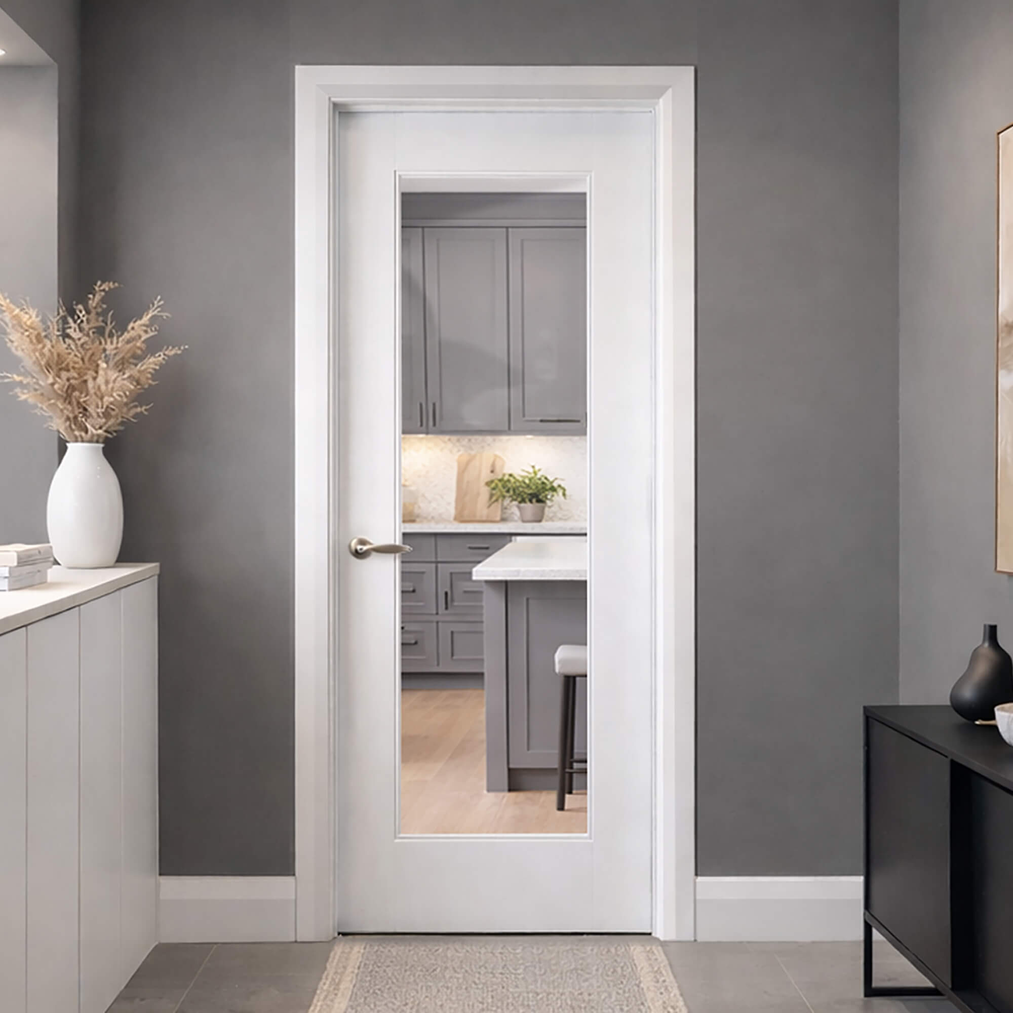 A Shaker White Primed 1 Lite Pre-Glazed Door in a hallway, with gray walls and furniture, looking into a kitchen setting.