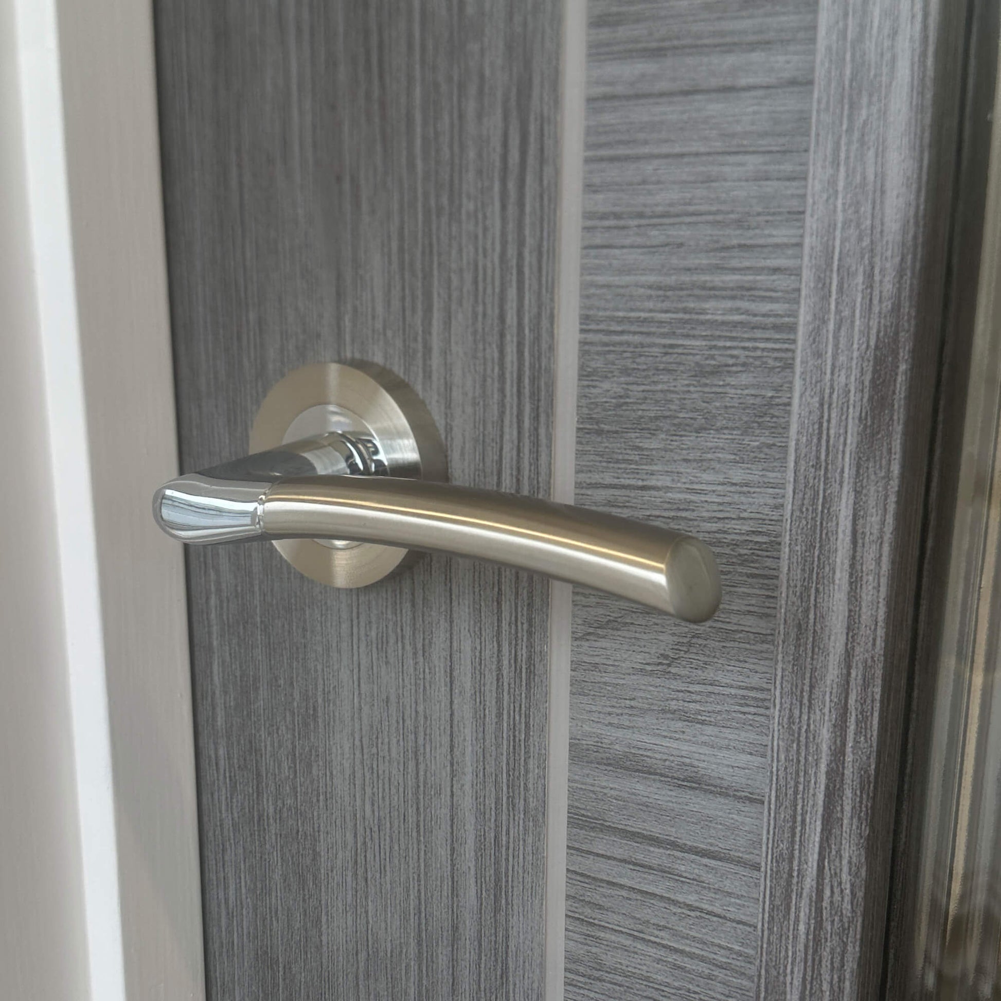 A close-up of a Storm Nickel Brushed & Polished Chrome door handle on a wooden door
