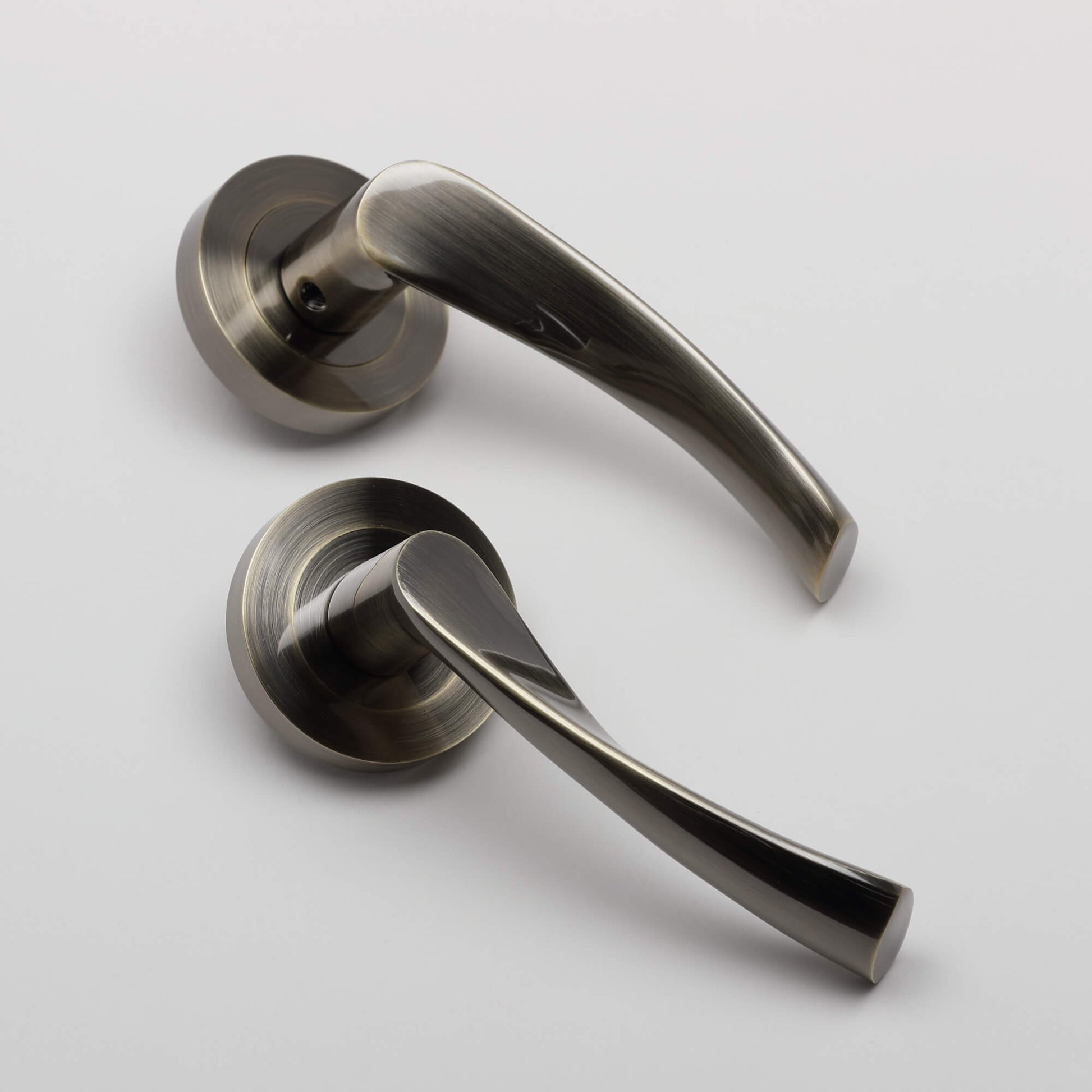 Angled view of a pair of Trade Range Antique Brass door handles on a grey background.