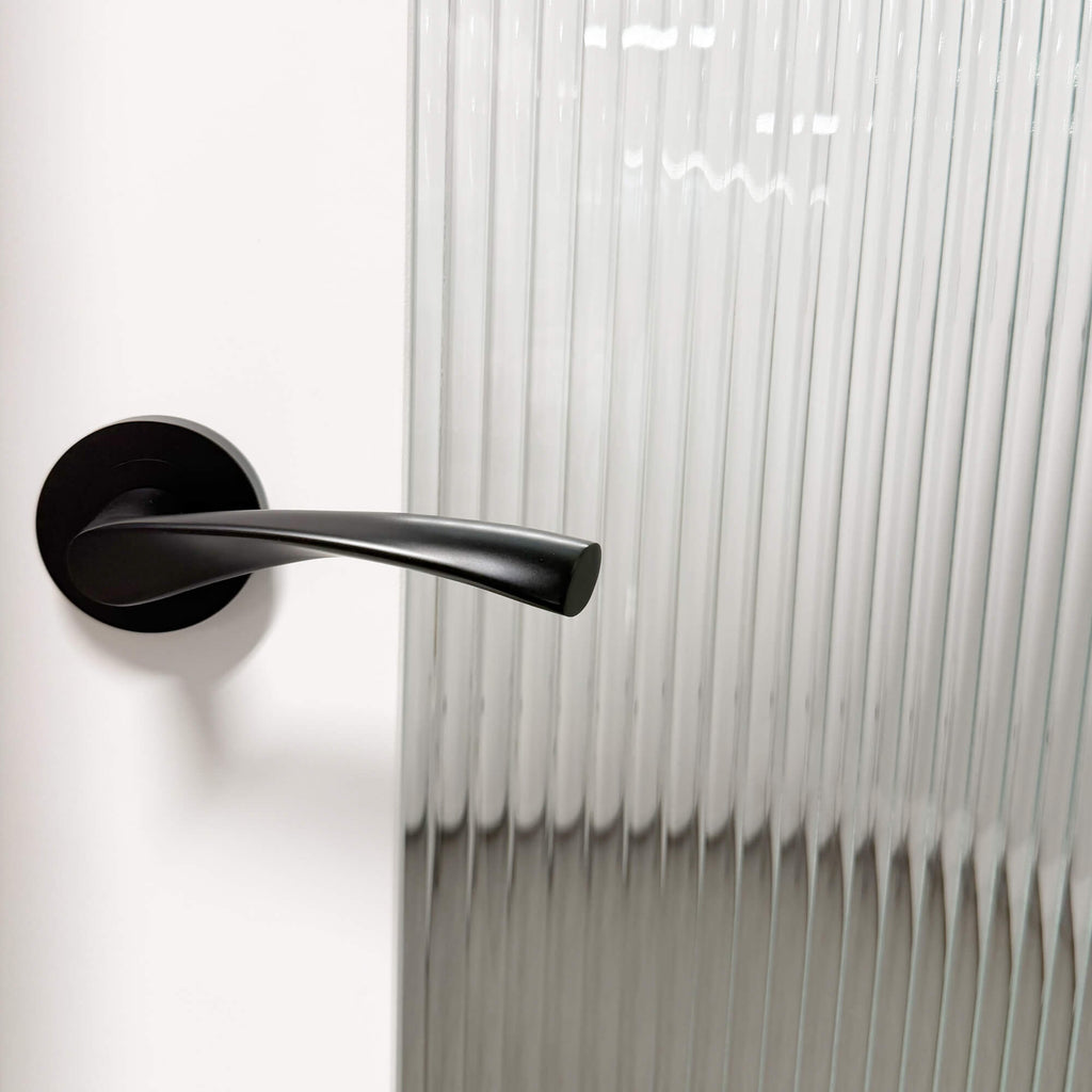 A Trade Range Flat Black door handle on a white door with a reeded glass panel