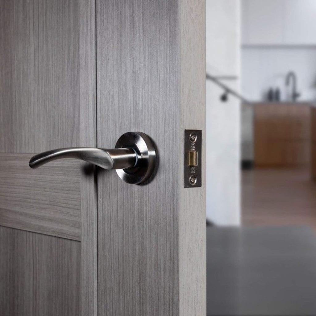 Close-up of a wooden door with a Trade Range Nickel Brushed & Polished Chrome Handle, with a blurred background.