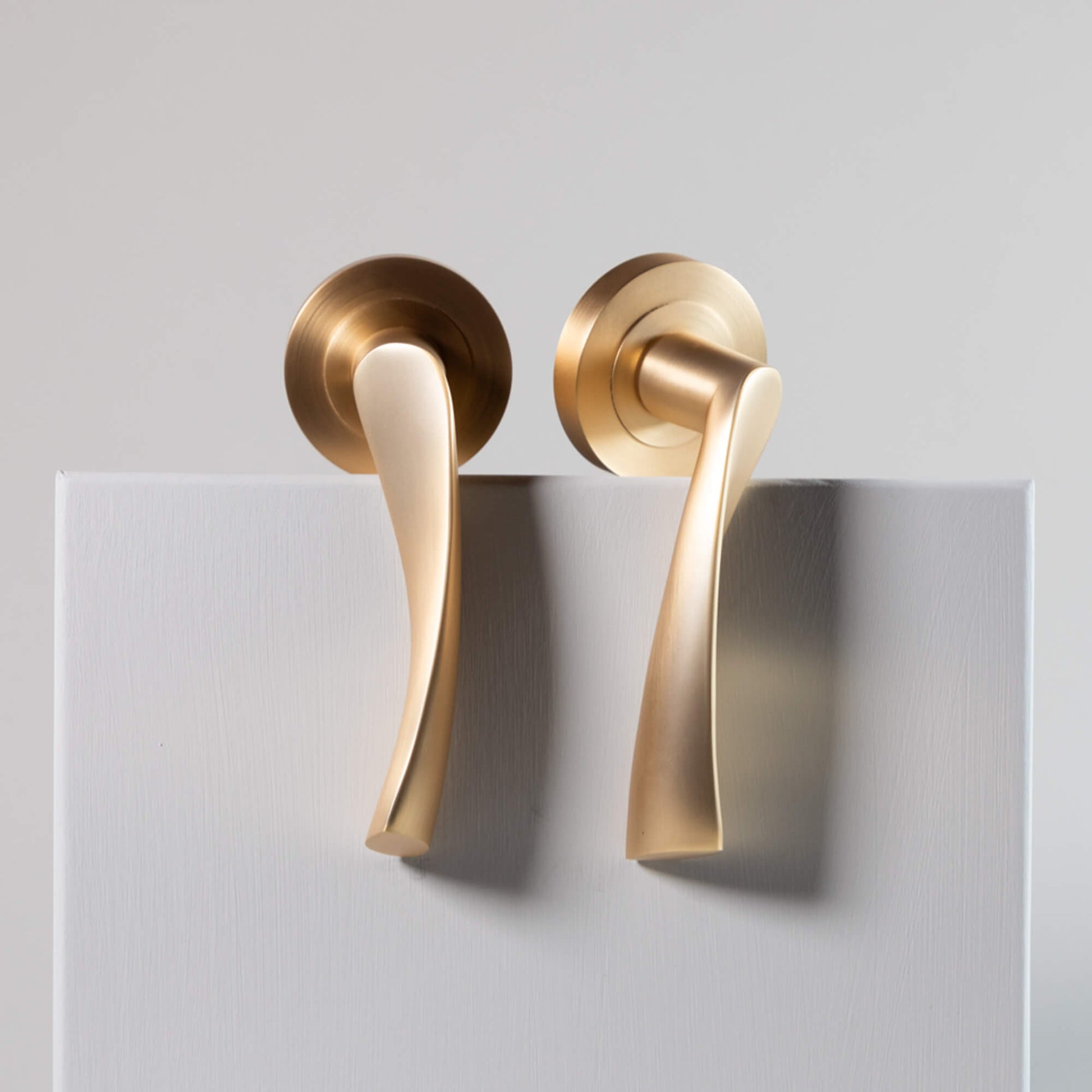 Pair of Trade Range Satin Brass door handles on a grey background.