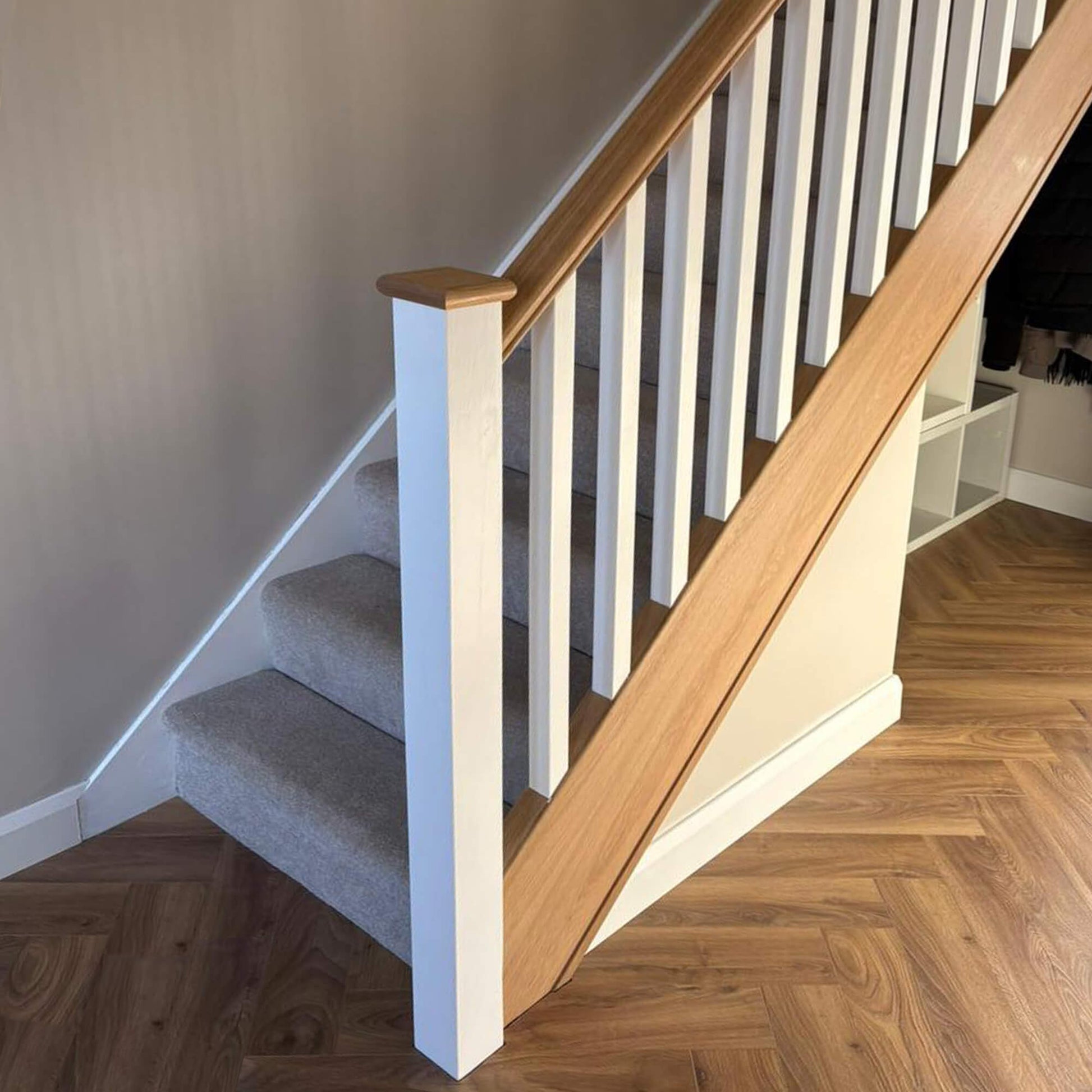 Staircase with wooden handrail and white primed blank spindles and blank newel post in a home interior setting.